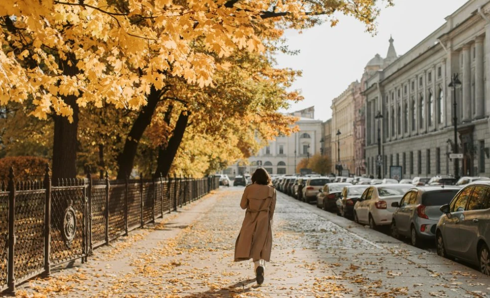 Mladá žena v béžovej oversized prechodnej bunde pozerá do objektívu na jesennej ulici