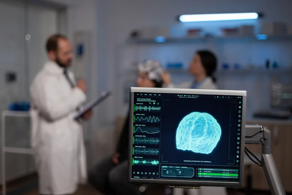 EEG vyšetrenie pacienta s elektródami na hlave a monitorom zobrazujúcim mozgovú aktivitu