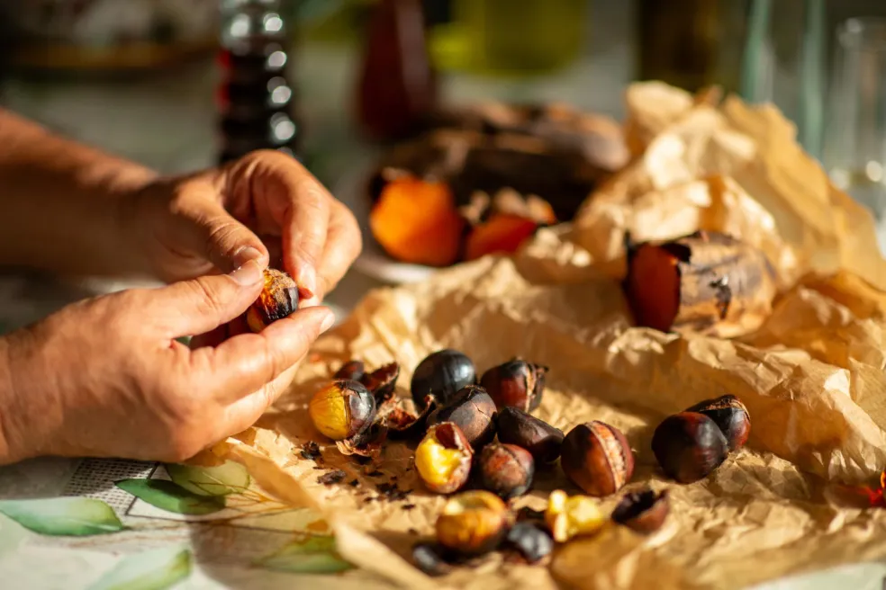 Jedlé gaštany s narezanou šupkou pripravené na pečenie v teplovzdušnej fritéze, drevená vareška na čiernom košíku.